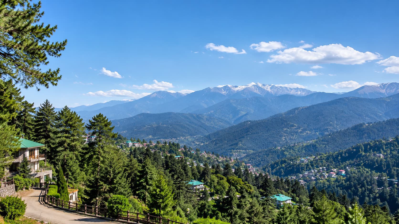 A sweeping view of the pine-forested valley and snow-capped peaks surrounding Chinar Resort